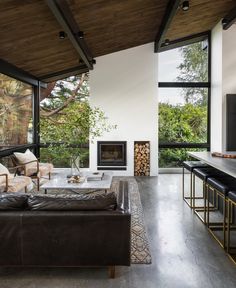 a living room with couches, tables and large windows overlooking the trees in the distance