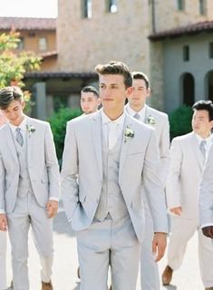 a group of men in white suits walking down a street with one man looking at the camera