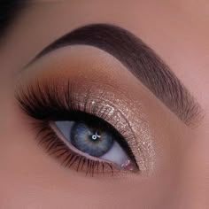 a woman's blue eye with long lashes and gold glitter on her eyeshadow