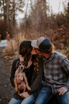 a man and woman sitting on the ground kissing while holding a dog in their lap