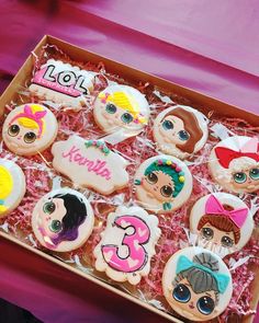 a box filled with lots of decorated cookies on top of a pink tablecloth covered table