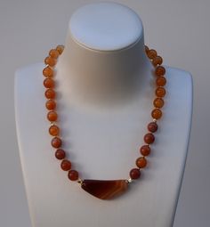 "Natural Carnelian Agate Necklace, 17 1/2\" Length, 10mm Smooth Round Agate with 44x18x8mm Asymmetrical Agate as a Center Piece, 2mm Gold Filled Spacer Round and Twisted Shape Beads, and Gold Plated Interlocking Clasp. Materials: Beads: Carnelian Agate, 10mm Shape: Smooth Round Center Piece: Carnelian Agate, 44x18x8mm Spacer Beads: Gold Filled Round, 2mm Spacer Beads: Gold Filled Twisted Shape, 4x5mm Clasp: Gold Plated Interlocking Carnelian Agate is known for its vibrant energy and metaphysical properties. This power stone stimulates ambition and drive, so it will aid you in manifesting what you require to move onto your desired path forward in life. It will aid you in making new, clearer decisions. By wearing Carnelian Agate jewelry, carrying the stone, and incorporating it into your spa Luxury Orange Agate Necklace, Desired Path, Carnelian Agate, Power Stone, Agate Jewelry, Agate Necklace, Spacer Beads, Gold Filled, Agate