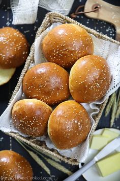 six buns with sesame seeds in a basket next to butter and cheese on a table