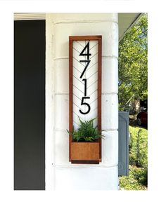 a house number sign mounted to the side of a building with a plant in it