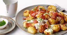 there is a plate of potatoes with bacon and sour cream on it next to a white cup