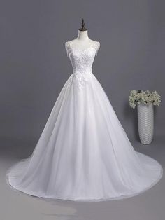 a white wedding dress on a mannequin next to a vase with flowers in it