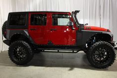 a red and black jeep parked in front of a white wall with curtains behind it