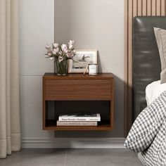 a nightstand with flowers and books on it next to a bed