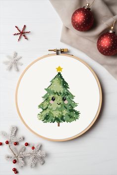 a cross stitch christmas tree on a white table next to red baubs and ornaments