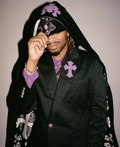 a man in a black suit and purple shirt is holding his face up to the camera