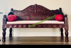 an ornate wooden bench with two red pillows on it's back rests against a white wall