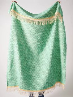 a green and white blanket with fringes hanging on a clothes rack in front of a wall