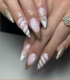 These stiletto nails feature a nude base with gold glitter tips and delicate white snowflake accents. The glitter adds a festive sparkle, while the snowflake design captures the winter feel. This look is perfect for those seeking long and glamorous winter nails. Gold And White Glitter Nails, Christmas Nails Acrylic Gold, White Gold Holiday Nails, Christmas Gold Nails Art Designs, Red And Gold Snowflake Nails, Holiday Nails White And Gold, Festive French Tips, Gold December Nails