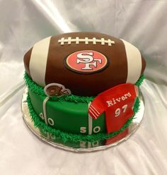 a football cake is decorated with green grass and red ribbon on the bottom tiers