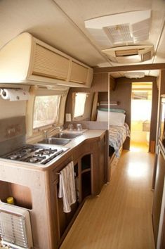 the interior of an rv with wood flooring and white counter tops, stove top oven and sink