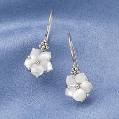 two white flowers are hanging from silver earwires on a blue cloth with beads