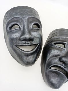 two masks with faces painted on them sitting next to each other in front of a white background