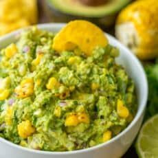 guacamole in a white bowl surrounded by avocados and limes