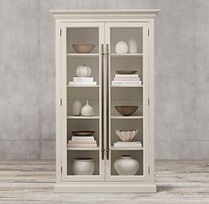 a white cabinet with glass doors and shelves filled with vases on top of it