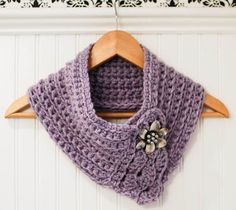 a purple crocheted scarf hanging on a wooden hanger next to a white wall