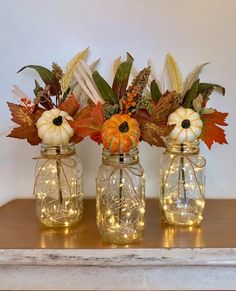 three mason jars filled with pumpkins, leaves and other autumn decorations sitting on a table