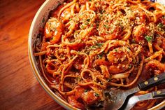 a bowl filled with pasta and sauce on top of a wooden table next to a fork