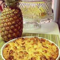 a pineapple sitting next to a pie on top of a table in front of a glass cake dish