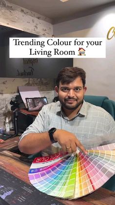 a man sitting in front of a desk holding up a color swatch with the words trending colours for your living room