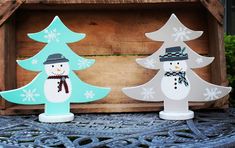 two snowmen standing next to each other in front of a wooden box with trees