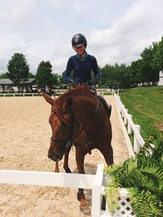 a man riding on the back of a brown horse over a white fence in an enclosed area