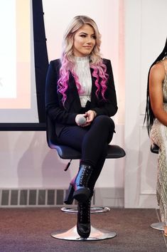 two women sitting on stools in front of a projector screen, one with pink hair