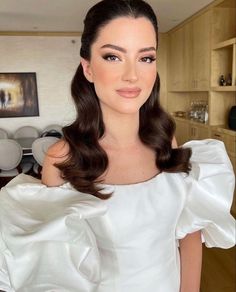 a woman in a white dress is posing for the camera with her hair styled into a half - up style