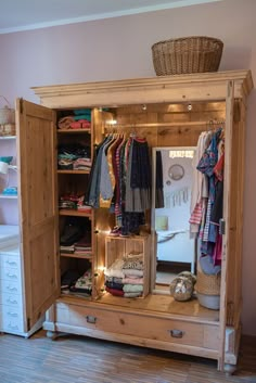 an open wooden cabinet with clothes hanging on the door and lights in the bottom drawer