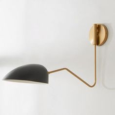 a black and gold wall light on a white wall next to a lamp shade that is shaped like a cone