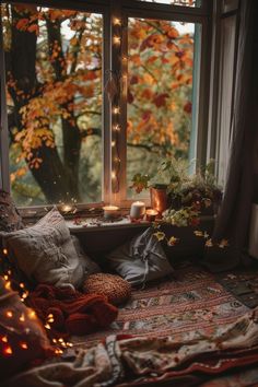 a window sill filled with lots of pillows and blankets next to a lit candle