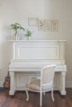 a white piano sitting on top of a hard wood floor next to a chair and potted plant