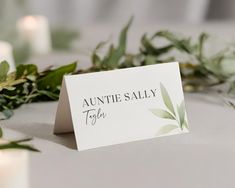 a place card sitting on top of a table with greenery around it and candles in the background