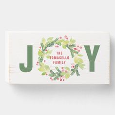 a wooden block with the words joy on it and holly wreaths in green lettering