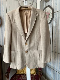 "This jacket is made from wool in timeless beige, in a fine herringbone pattern. It has the original turtle buttons in the front and on the cuffs, two front pockets and two inside pockets, and it's partially lined with tan silky lining. The label reads \"Tailored Especially for The Men's Shop Claremore Okla.\" The measurements, taken with the jacket lying flat, are: shoulder to shoulder, 18 inches; armpit to armpit, 20 inches; sleeves, 25 inches; length, 31 1/2 inches; bottom edge, 25 inches. In very good condition." Beige Tweed Jacket With Lapel Collar For Semi-formal Occasions, Beige Long Sleeve Tweed Jacket For Semi-formal Occasions, Beige Winter Suit With Lapel Collar, Fitted Beige Sport Coat For Winter, Fall Beige Suits With Buttons, Beige Fall Suits, Tailored Beige Tweed Jacket For Business Casual, Tailored Beige Tweed Jacket With Lapel Collar, Beige Notch Lapel Tweed Jacket For Business