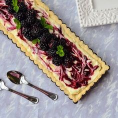 a pastry with berries and mint on it next to spoons, fork and knife