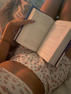 a woman laying in bed with her legs crossed and holding an open book over her stomach