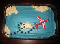 a cake that is shaped like an airplane with clouds in the sky and blue icing