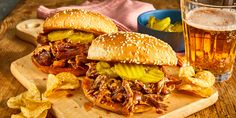 two pulled pork sandwiches with pickles and onions on a cutting board next to chips