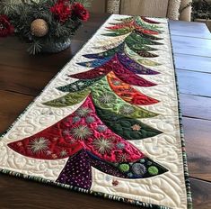 a christmas tree table runner on a wooden table next to a vase with red flowers