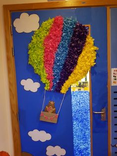 a door decorated with tissue flowers and a hot air balloon in the shape of a rainbow