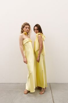 two women in yellow dresses standing next to each other with their hands on their hips