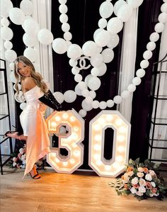 a woman standing in front of a large number with balloons and flowers on the floor