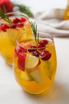 two glasses filled with fruit and veggies on top of a white tablecloth