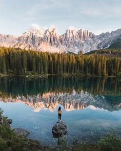 a person standing on top of a rock next to a lake with mountains in the background