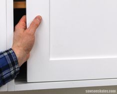 a person's hand on the door handle of a white cabinet